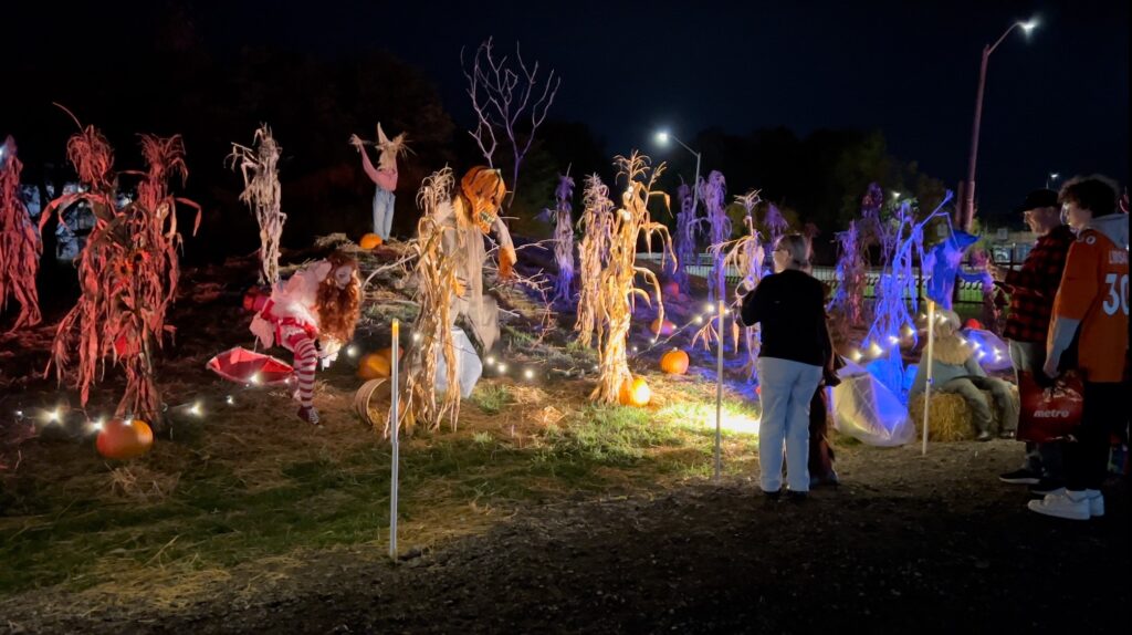 Visitors exploring Halloween figures and illuminated cornstalks in the Village Field
