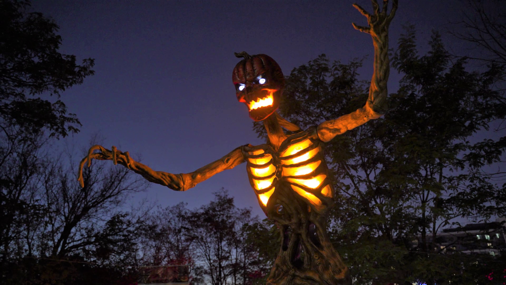 A towering pumpkin figure glowing against the evening sky at the Village